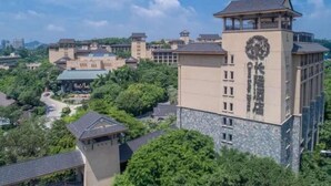 A multi-story building with a clock tower, surrounded by greenery and other buildings. - Chimelong Hotel (Guangzhou)
