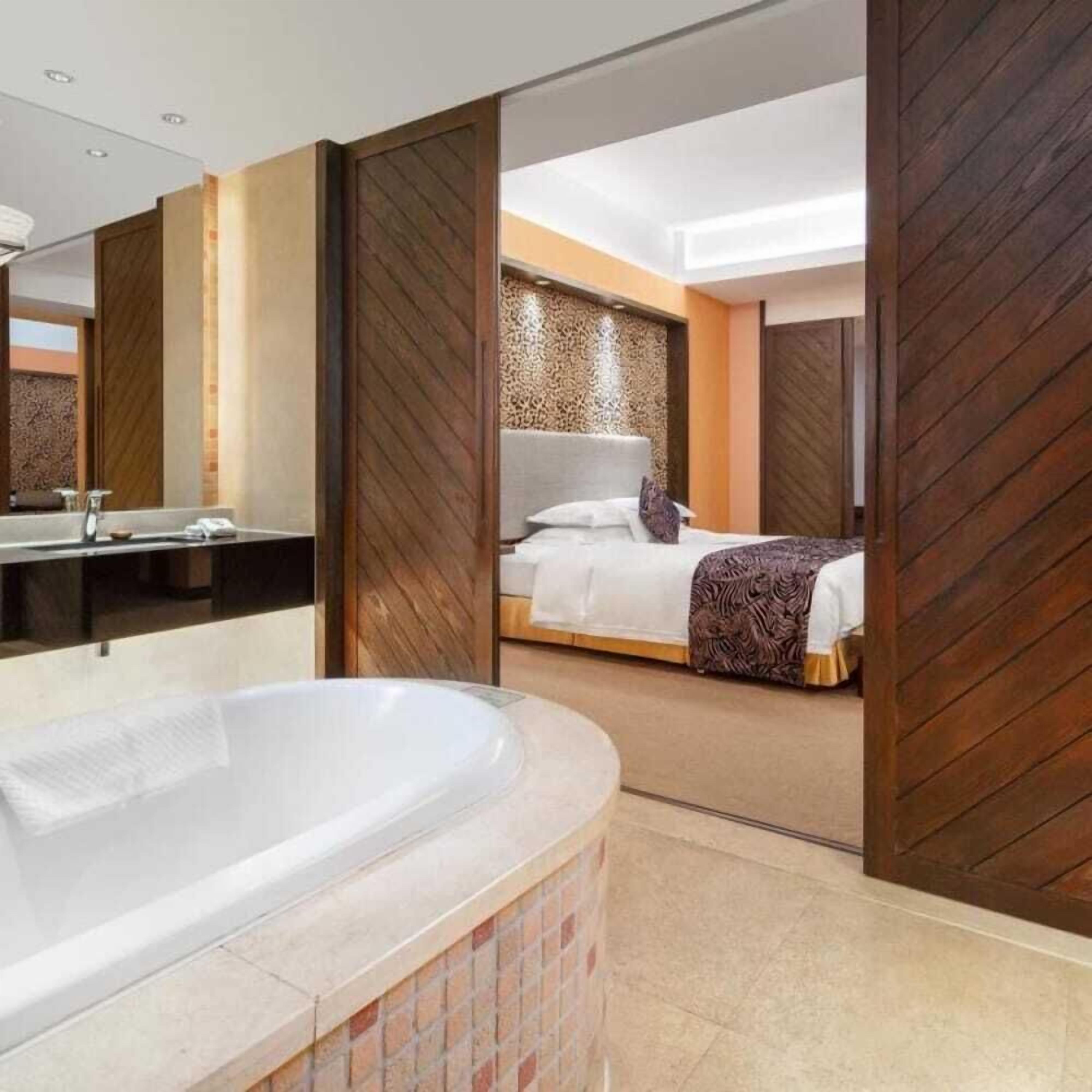 Un baño moderno con una bañera grande, un área de ducha independiente y un dormitorio con cama y una manta decorativa.