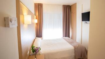 A hotel room with a bed, bedside table, lamp, curtains, and a TV mounted on the wall.