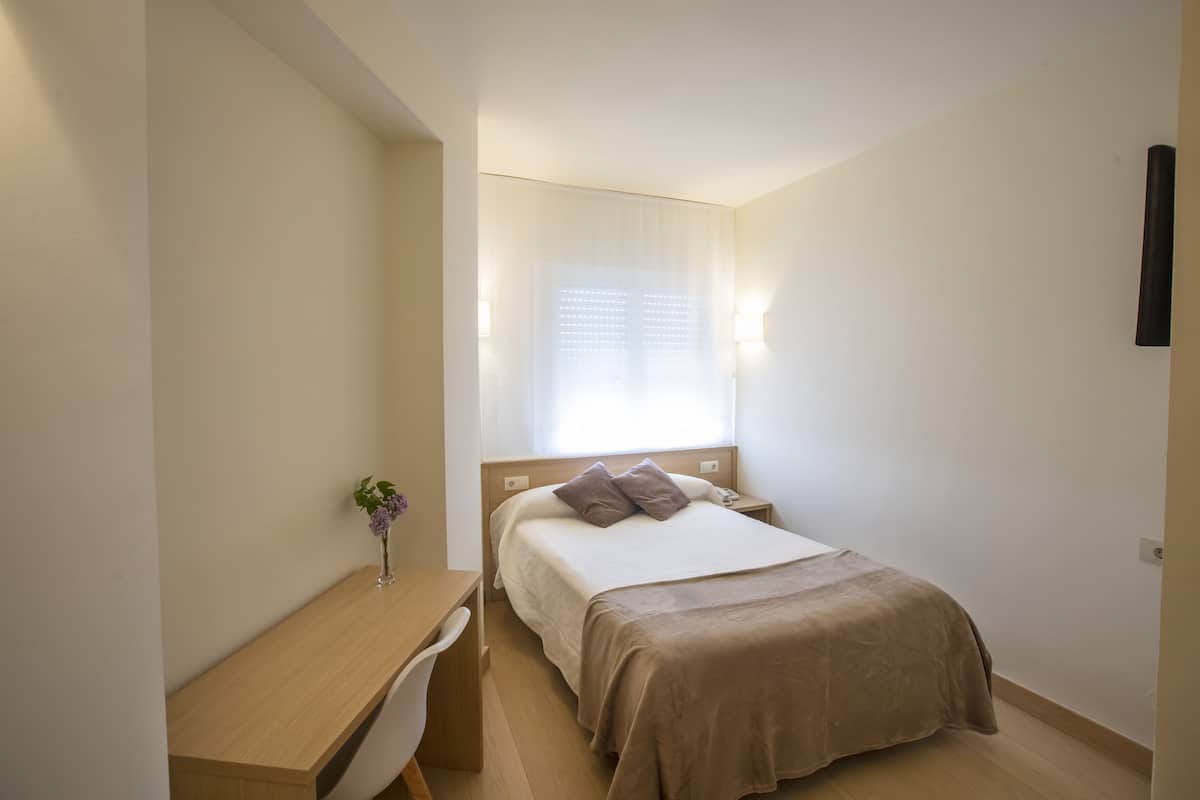 A bedroom with a bed, bedside table, chair, and a small desk.