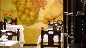 Comedor con una mesa dispuesta para dos, una silla y un mural en la pared que representa un cuenco de fruta.
