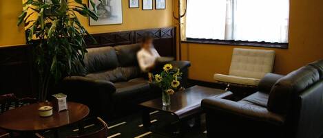 A cozy room with a sofa, armchair, and a dining table. There is a television mounted on the wall and a large window with curtains.