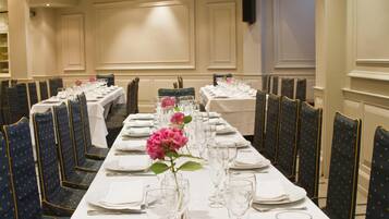 Ein langer Festsaal-Tisch mit Stühlen, jeder Tisch mit einer weißen Tischdecke und einer rosa Blumenarrangements.