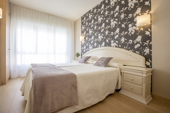 A bedroom with a large bed, a nightstand, a wall-mounted lamp, and a window with sheer curtains. - Hotel Ciudad De Calahorra (Calahorra)