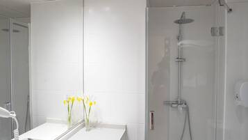 A modern bathroom with a glass-enclosed shower, a white vanity with a mirror, and a vase with yellow flowers.