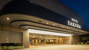 Une entrée d’hôtel moderne, dotée d’une façade incurvée et sur laquelle le nom « Hôtel Sakura » est clairement affiché.