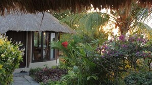 A thatched-roof structure with a glass door, surrounded by lush tropical vegetation and a stone pathway. - Coconut Beach Resort (BALI)