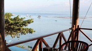 A wooden table with chairs on a balcony overlooking a body of water with boats. - Coconut Beach Resort (BALI)