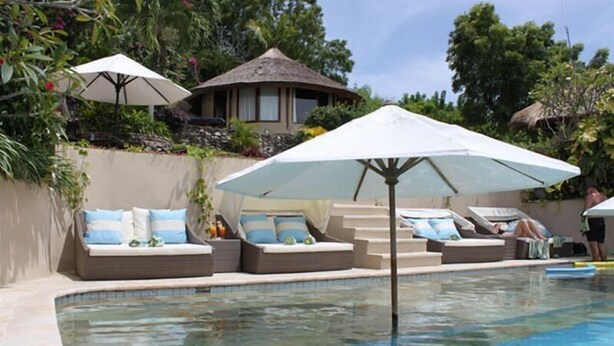 A pool area with lounge chairs and umbrellas, surrounded by greenery and a small building. - Coconut Beach Resort (BALI)