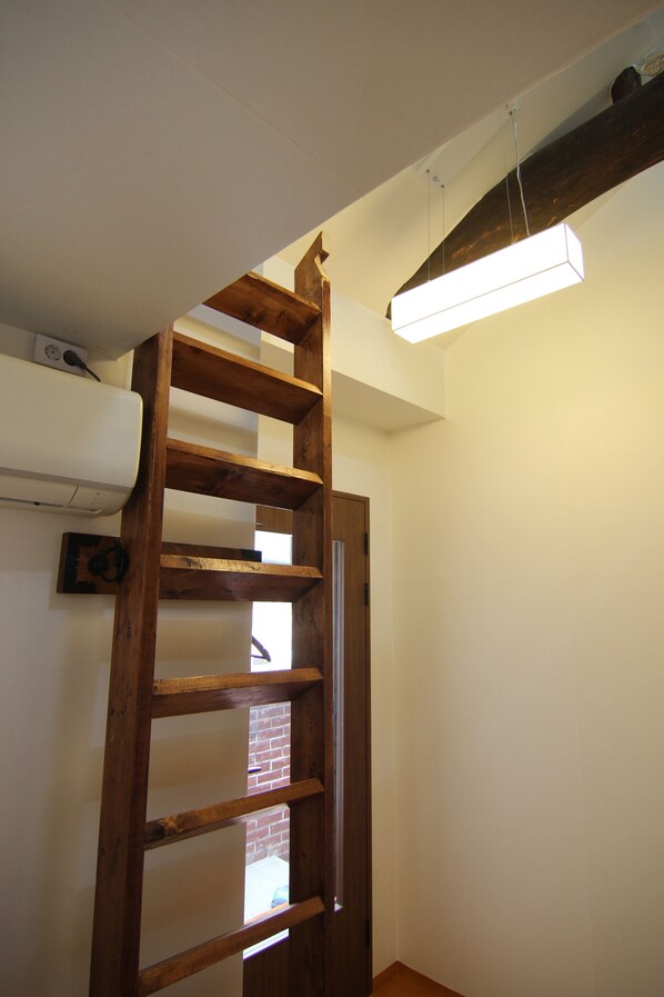 A wooden ladder in a room with a white ceiling and a hanging light fixture.