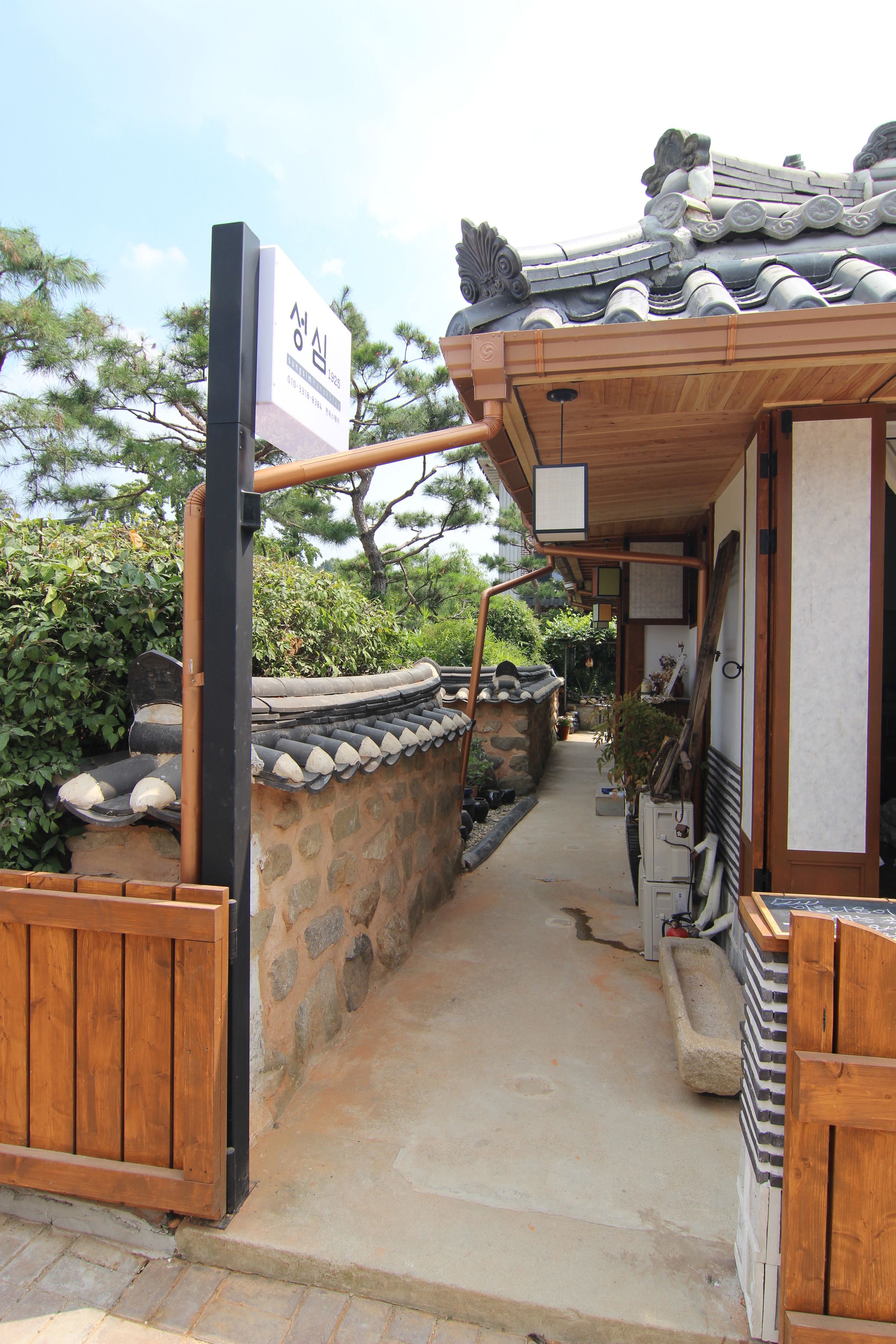 A traditional Korean gate with a wooden structure and stone wall, leading to a pathway.