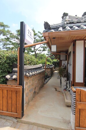 A traditional Korean gate with a wooden structure and stone wall, leading to a pathway. - Sungsim (Jeonju)