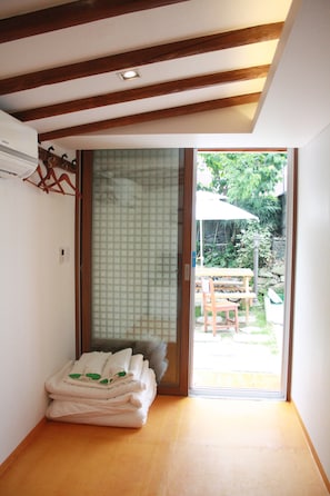 A room with a sliding glass door leading to an outdoor area, a wooden floor, and a stack of folded towels. - Sungsim (Jeonju)