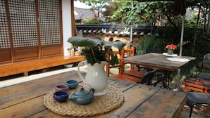 A wooden table with a woven placemat, a white pitcher with flowers, and two teapots. - Sungsim (Jeonju)