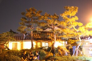 A traditional building with a tiled roof and a well-maintained garden with pine trees.