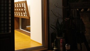 A room with a wooden ceiling, a sliding door leading to another space, a small table with a bottle and a glass, and a potted plant. - Sungsim (Jeonju)