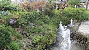 A traditional Japanese garden with a small waterfall, lush greenery, and a stone pathway. - Sungsim (Jeonju)