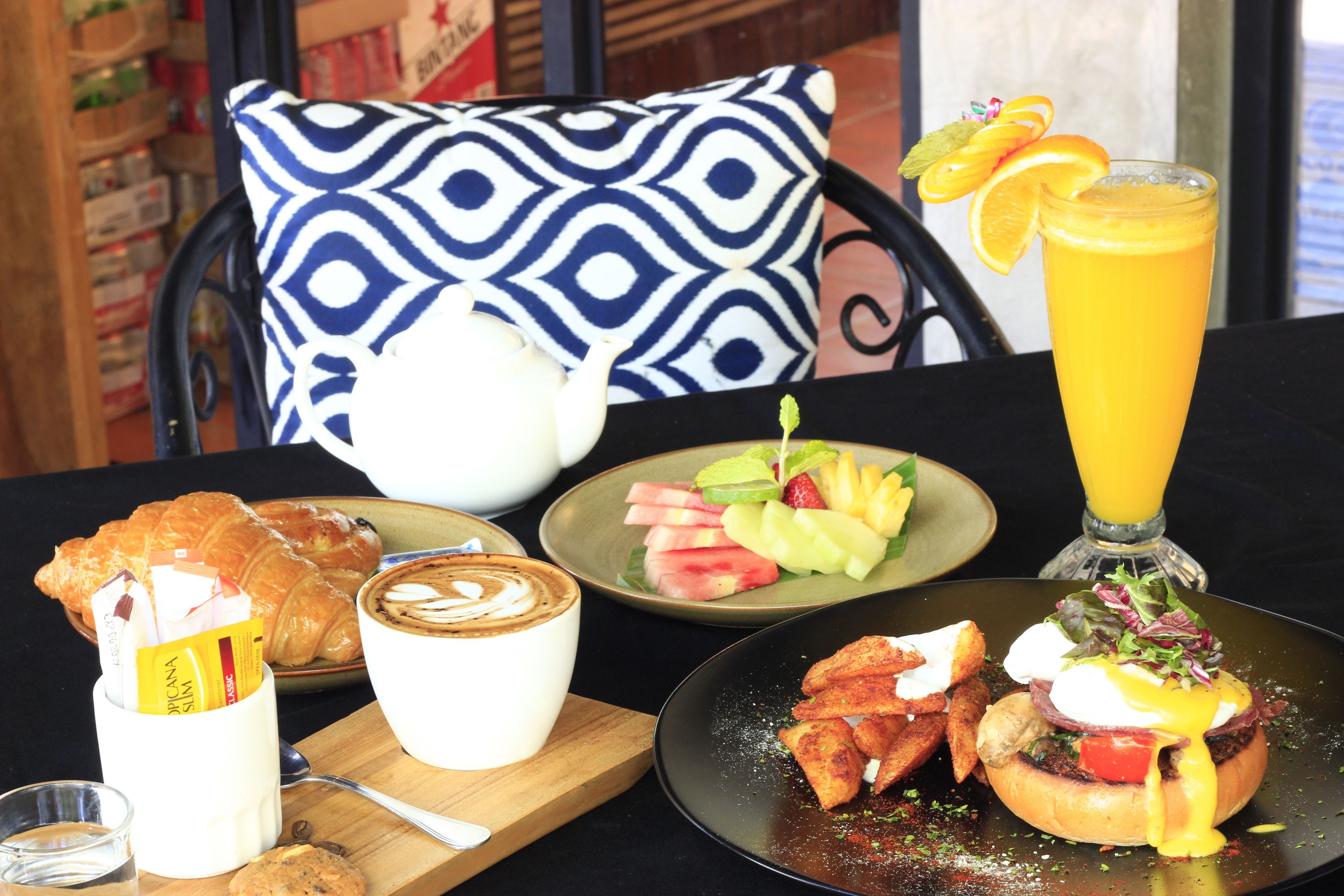 A breakfast setting with croissants, coffee, fruit salad, a burger, and a glass of orange juice.