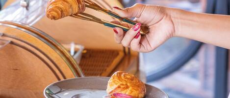 Iemand houdt een croissant en een gebakje vast, met een houten toonbank en een marmeren vloer.