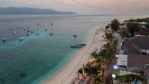 A beachside hotel with a view of the sea, boats, and a restaurant along the shore.