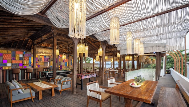 An outdoor wooden deck with seating, hanging lights, and a colorful wall in the background.