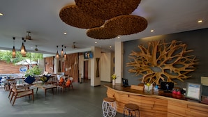 A modern reception area with wooden furniture, a large tree bark wall art, and multiple hanging light fixtures.