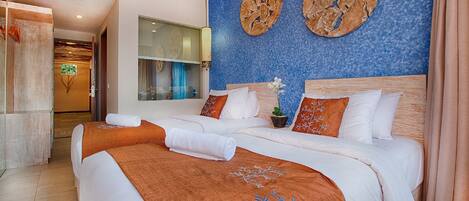Quarto de hotel com duas camas, uma janela grande, arte decorativa na parede e um vaso de planta.