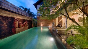 A pool area with a wooden deck, a lounge chair, and a wall with decorative items.