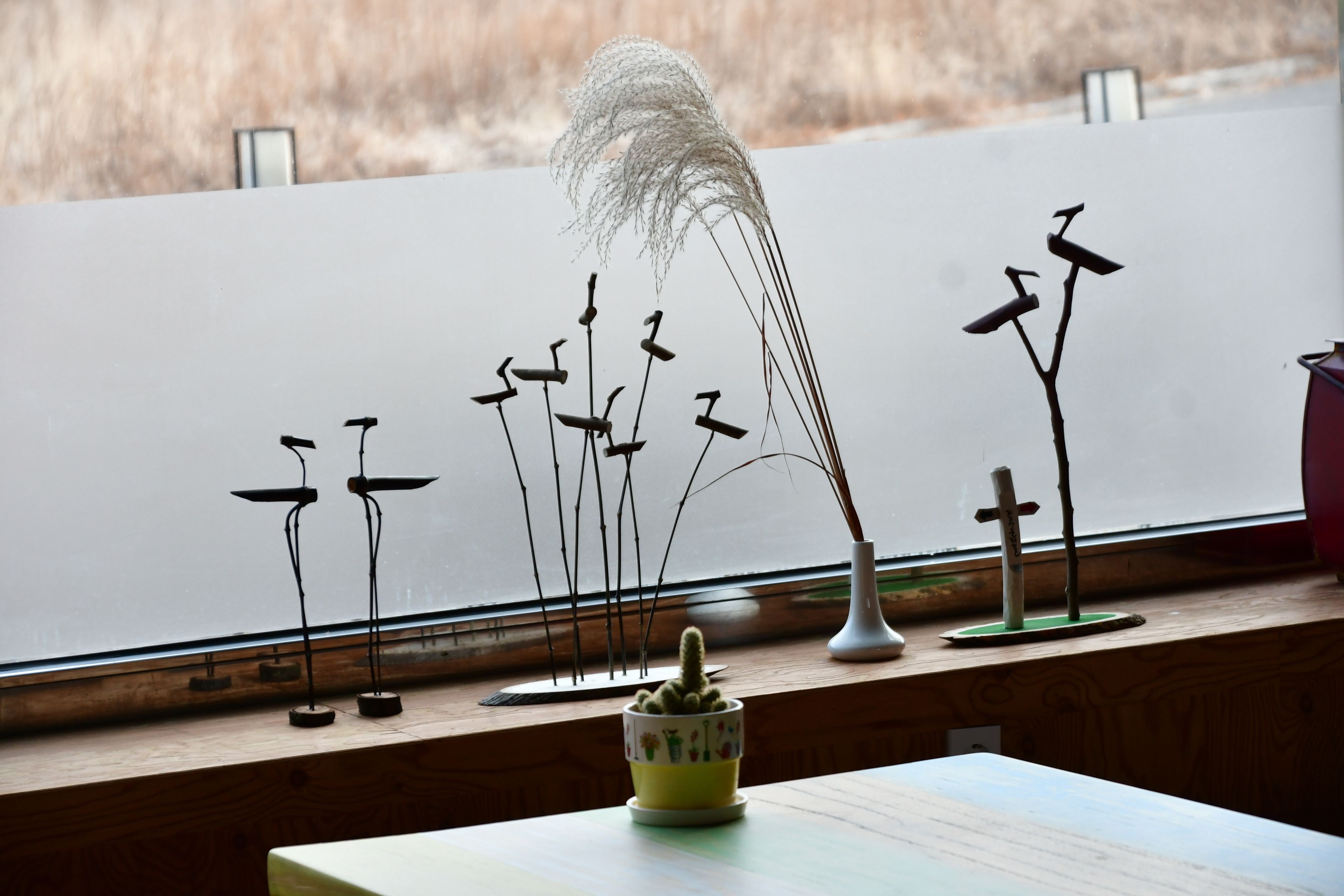 A table with a potted cactus, a decorative plant, and a small sculpture.