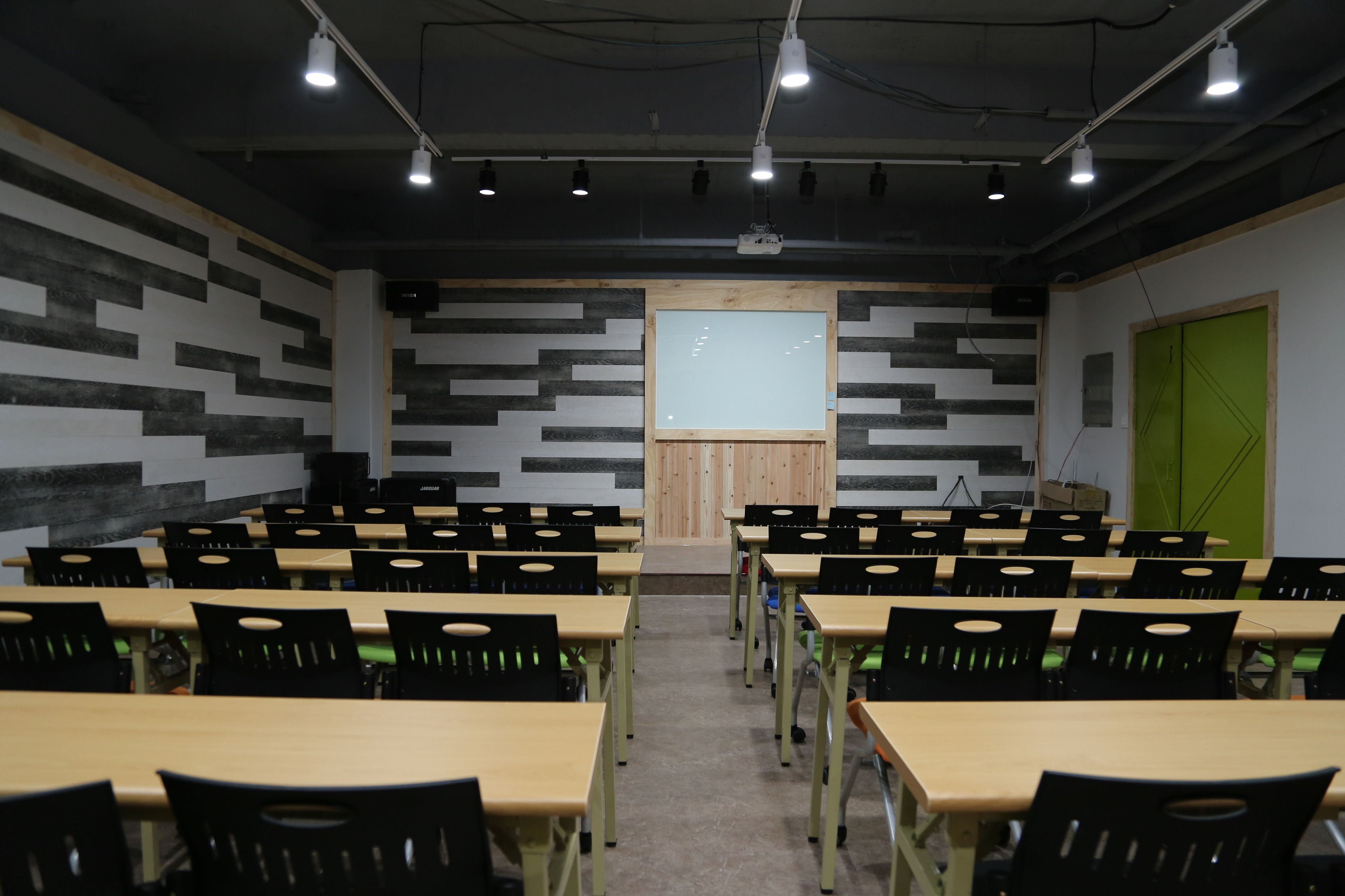 Una sala conferenze con diversi tavoli e sedie, uno schermo per proiettore e una porta verde.