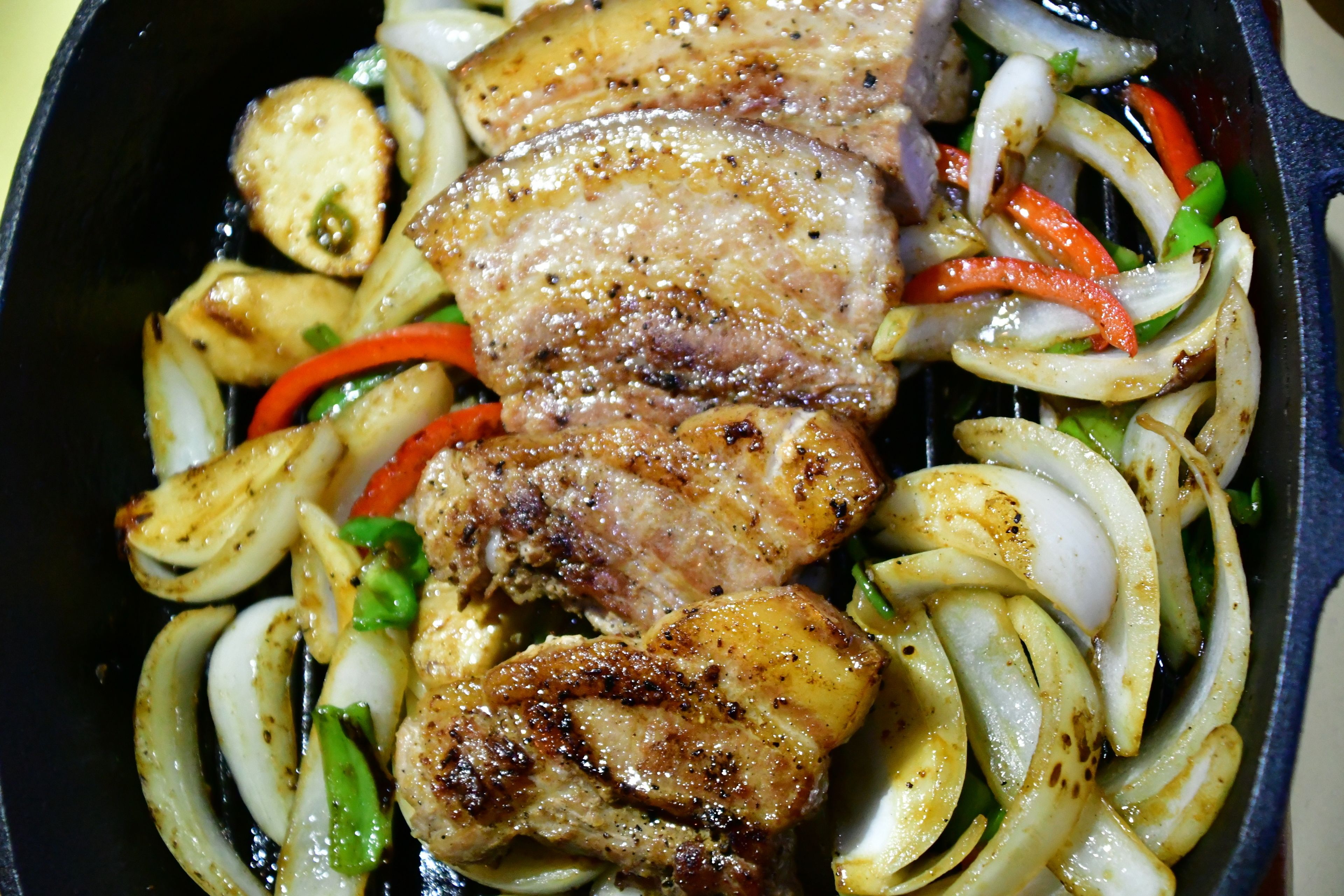 Una sartén con chuletas de cerdo a la parrilla, cebollas y pimientos.