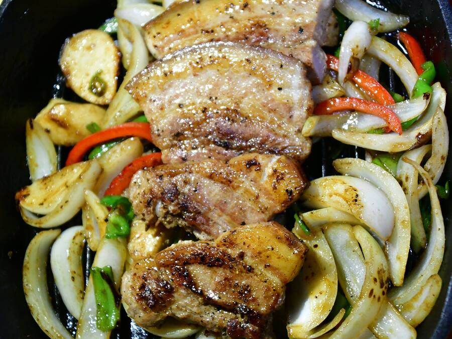 A skillet with grilled pork chops, onions, and bell peppers.