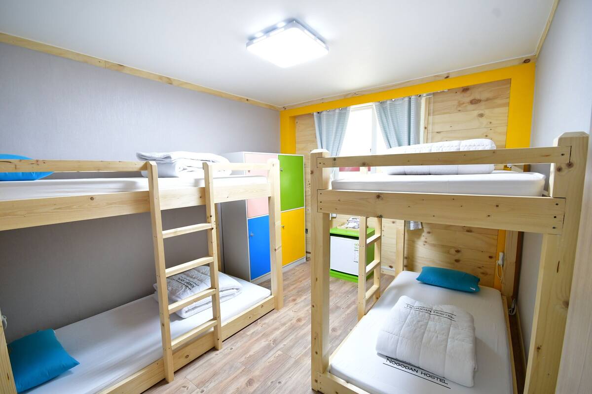 Ein Schlafraum mit Etagenbetten, Holzboden, Schreibtisch und Kleiderschrank.