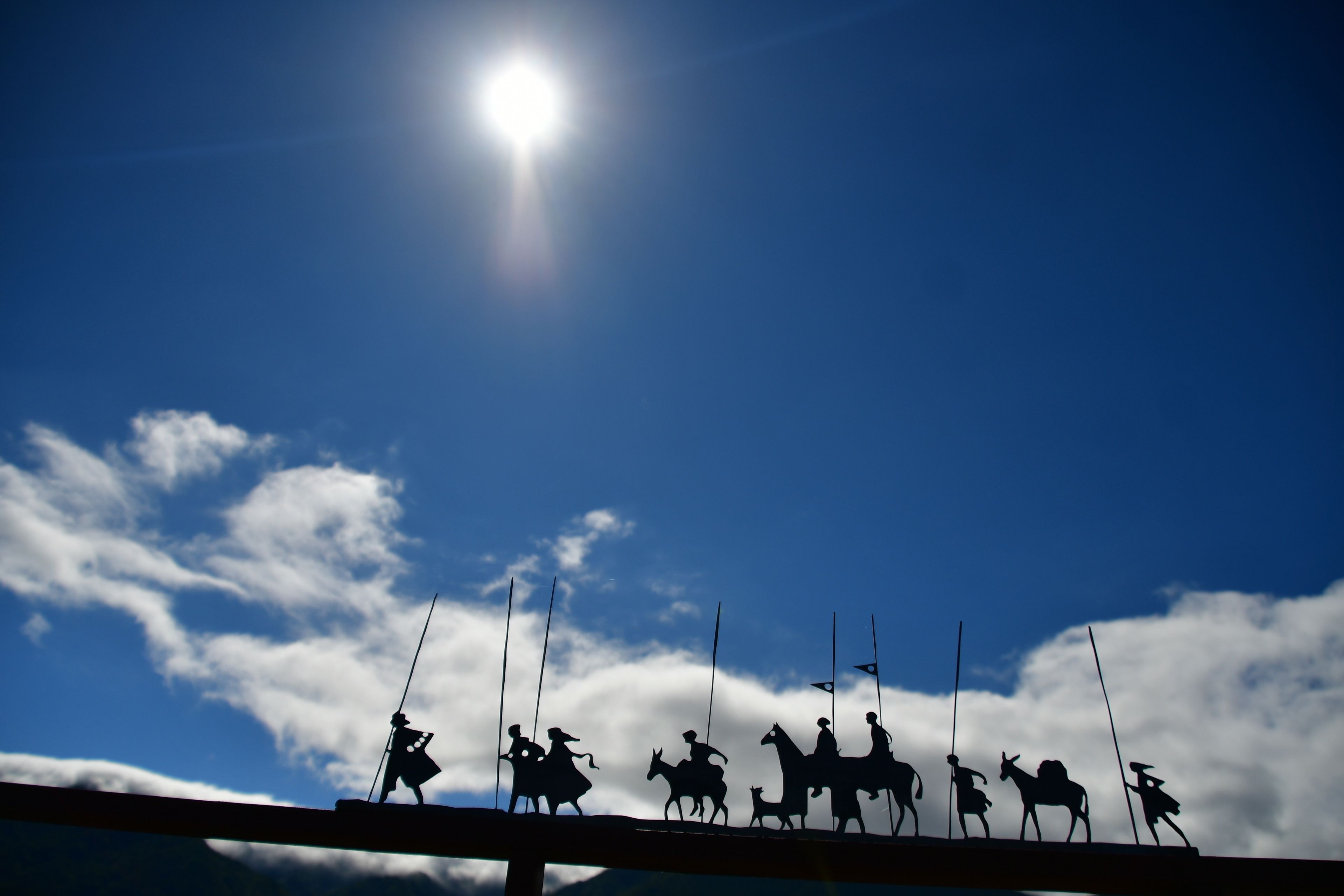 A silhouette of a group of people on horseback against a bright sky with clouds.