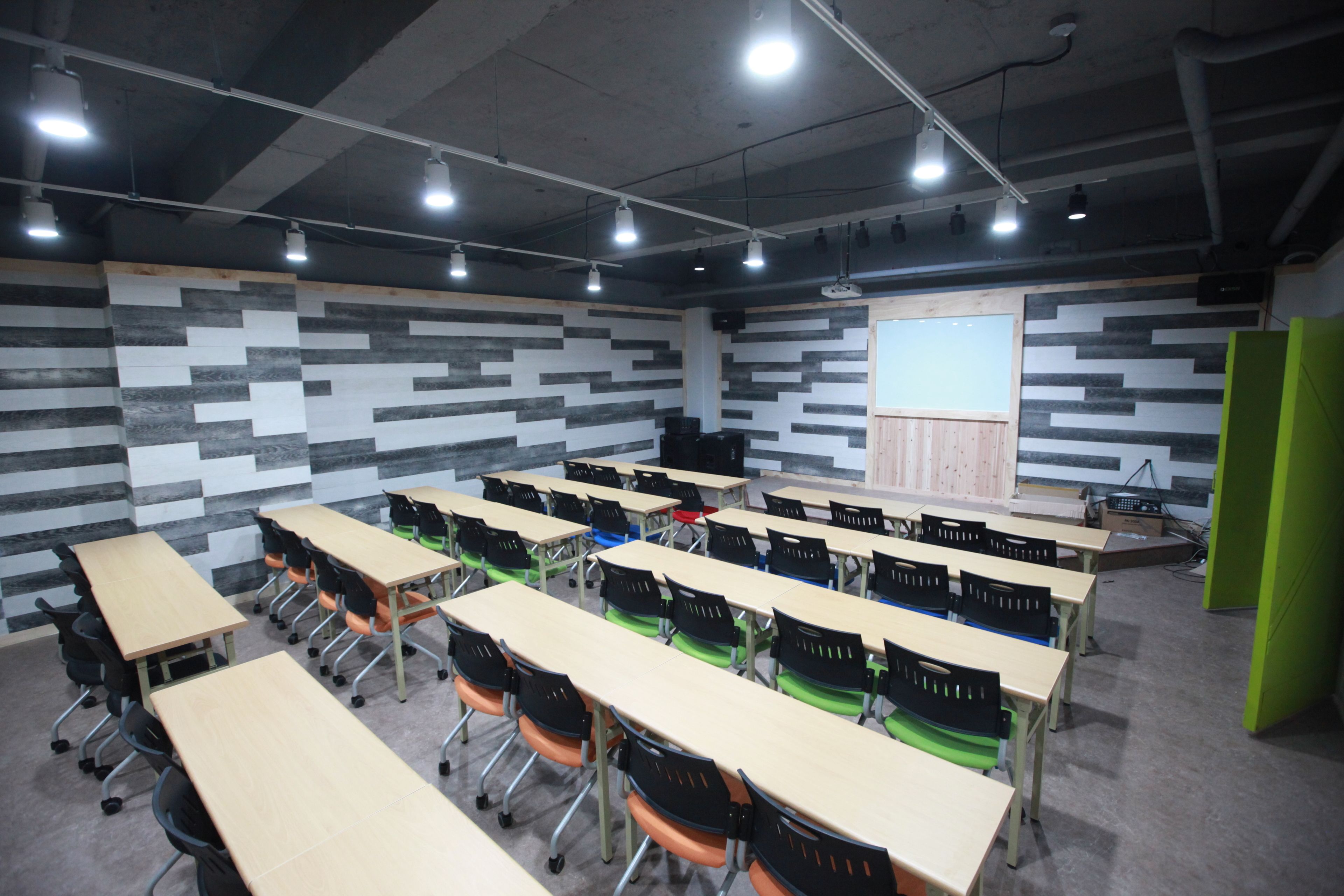 Ein Klassenzimmer mit Reihen von Schreibtischen und Stühlen, einer Projektionsleinwand und einer Tafel.
