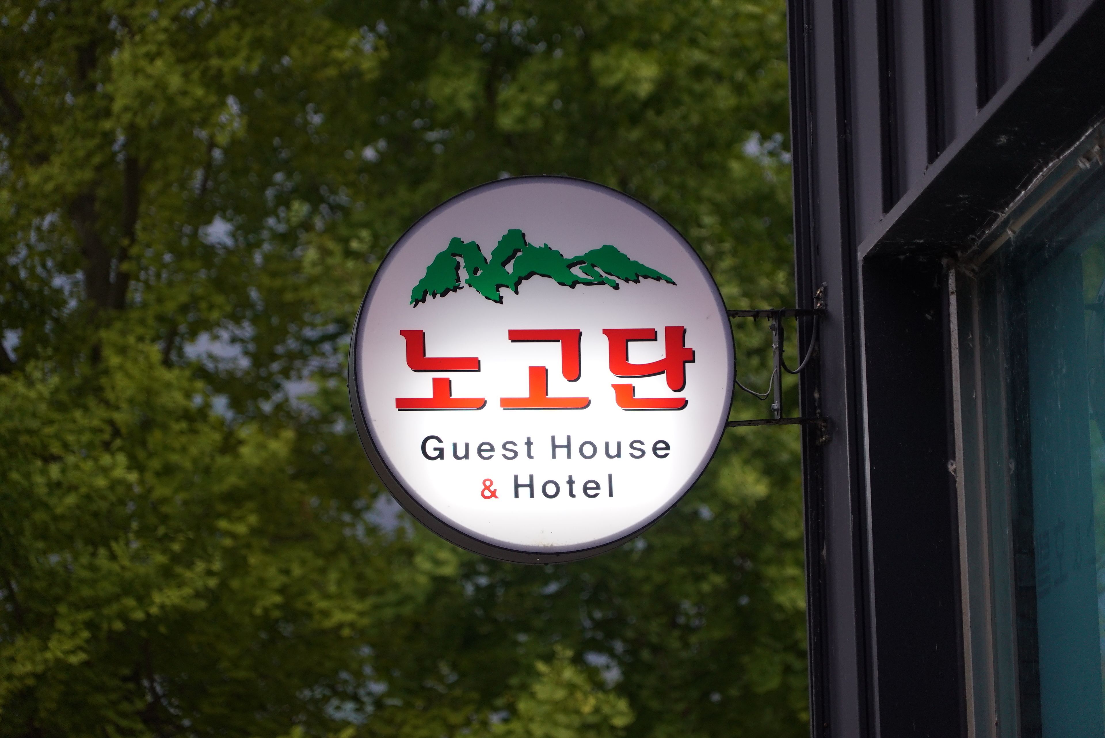 A circular sign with Korean text and a mountain graphic, indicating a guest house and hotel.