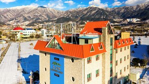 Un hotel con techo rojo y letrero azul, rodeado de montañas nevadas.