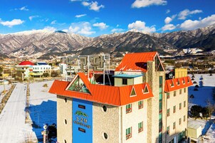 Un hotel con techo rojo y letrero azul, rodeado de montañas nevadas.