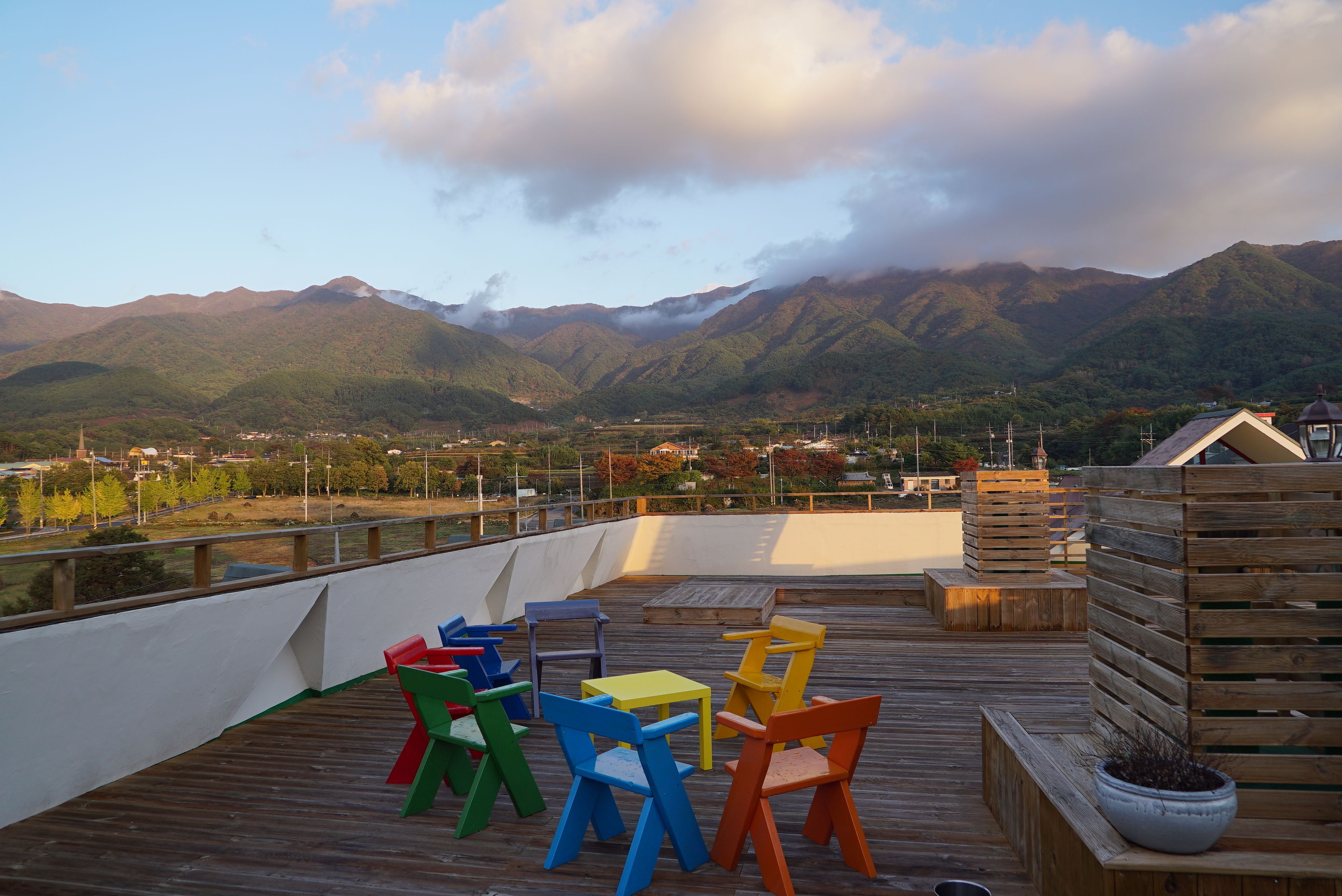 Une terrasse en bois, agrémentée de chaises et de tables aux couleurs vives, qui offre une vue sur un paysage montagneux.