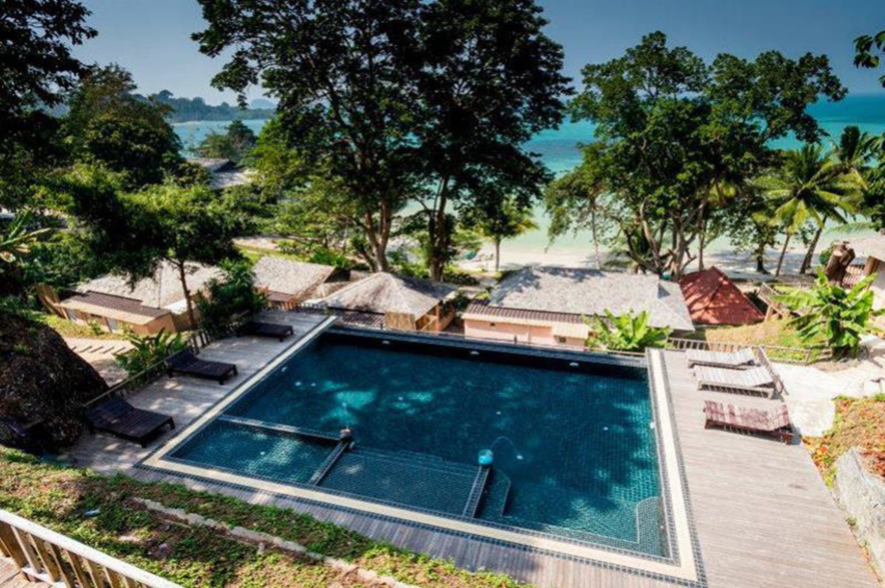 Un área de piscina con sillas de descanso, una terraza de madera y vistas a la playa y al océano.