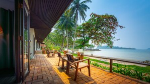 Une terrasse meublée de mobilier en bois, donnant sur une plage et des palmiers.