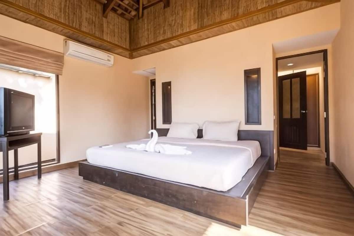 Quarto com uma cama grande, televisão sobre um suporte e teto de madeira.