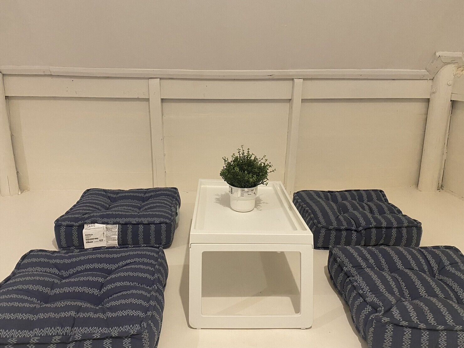 Ein Zimmer mit einem weißen Tisch, vier gemusterten Kissen und einer Topfpflanze.