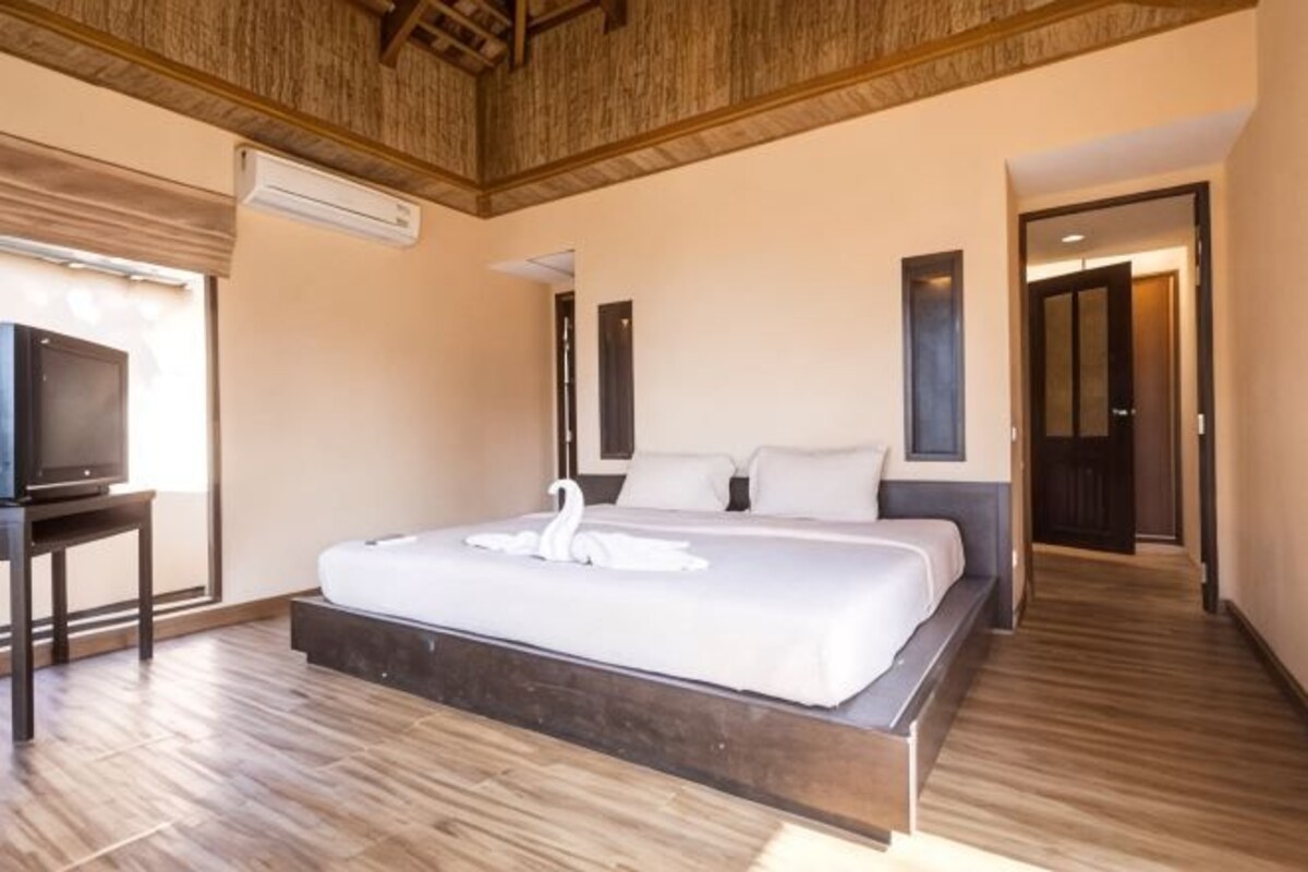 A bedroom with a large bed, a television on a stand, and a wooden ceiling.