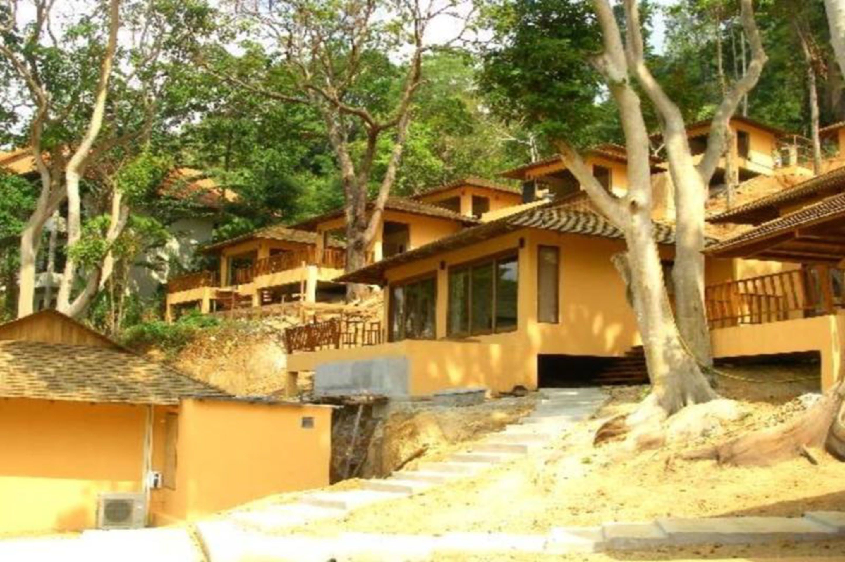A row of yellow buildings with multiple balconies, surrounded by trees.