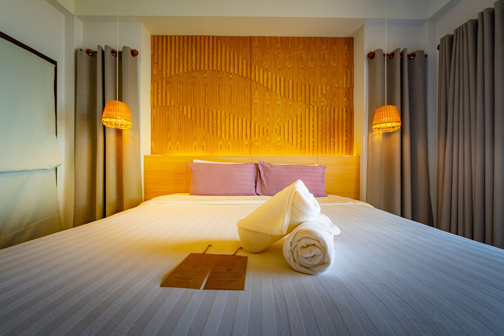 Ein Hotelzimmer mit einem großen Bett, einem Holz-Kopfende, zwei Wandlampen und einem ordentlich bezogenen Bett mit einem zusammengerollten Handtuch und einer Speisekarte.