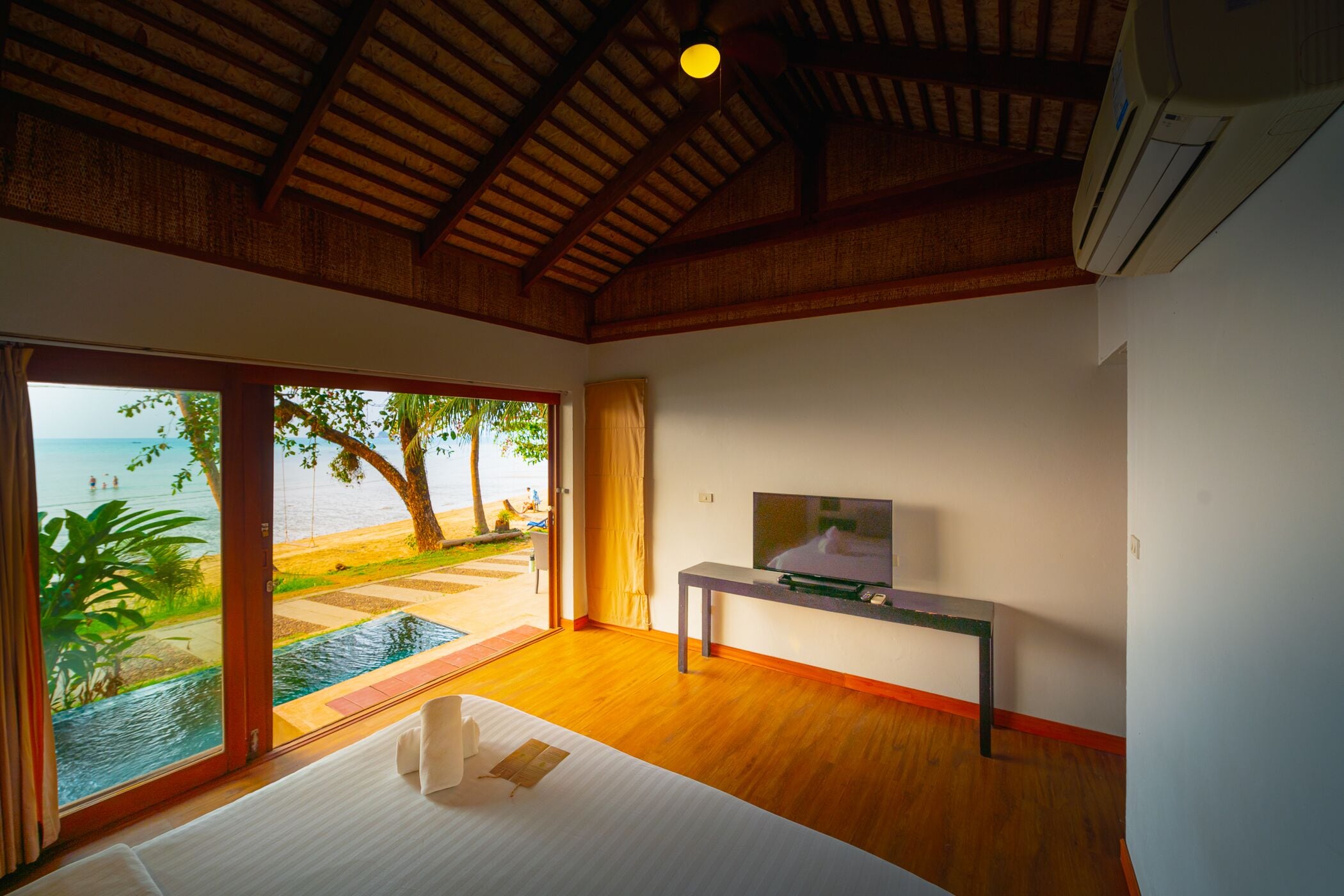 Habitación de hotel con techo de madera, una cama, un televisor y vistas a la playa.