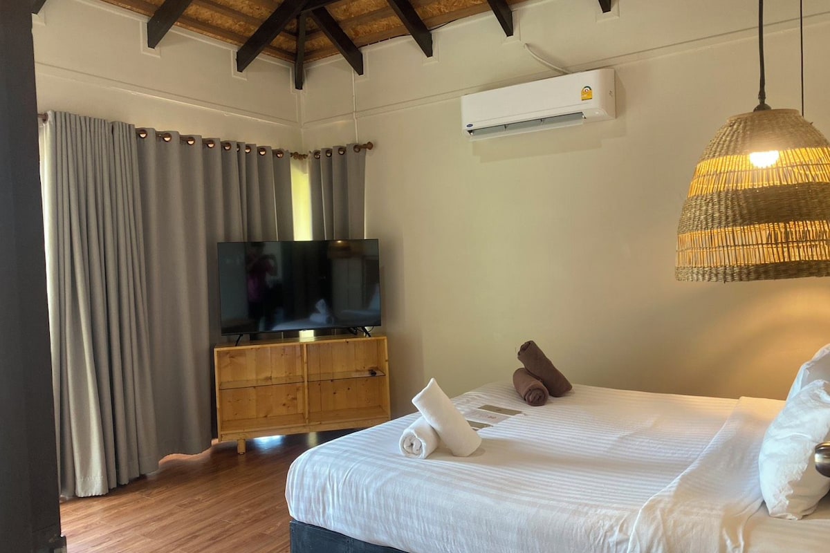 Quarto de hotel com cama, televisão, armário de madeira e ventilador de teto.