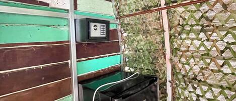 A room with a green and brown striped wall, a small window with a circular mirror, a wall-mounted electrical outlet, and a black appliance on the floor.