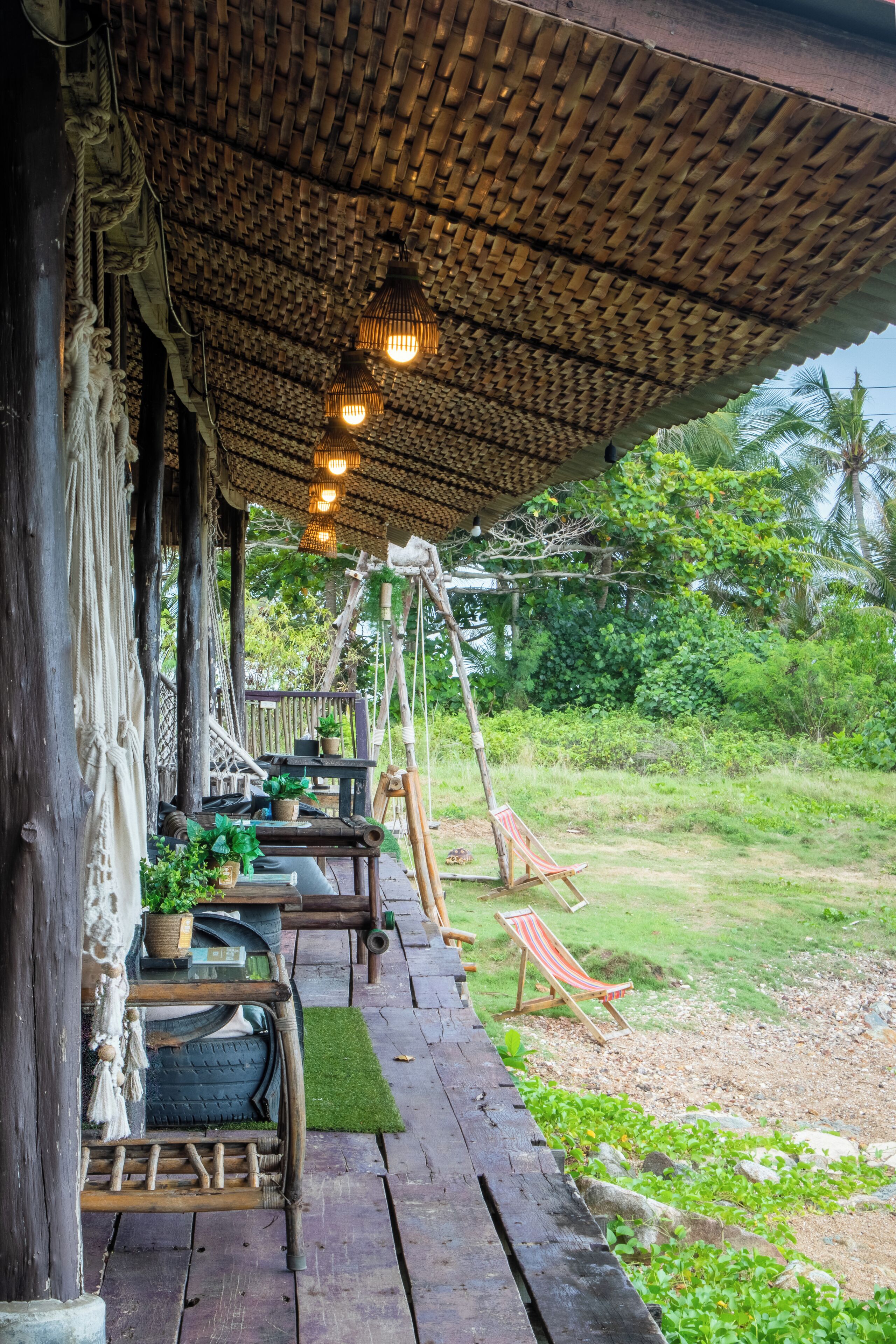 A wooden deck with a thatched roof, outdoor seating, and a swing set.